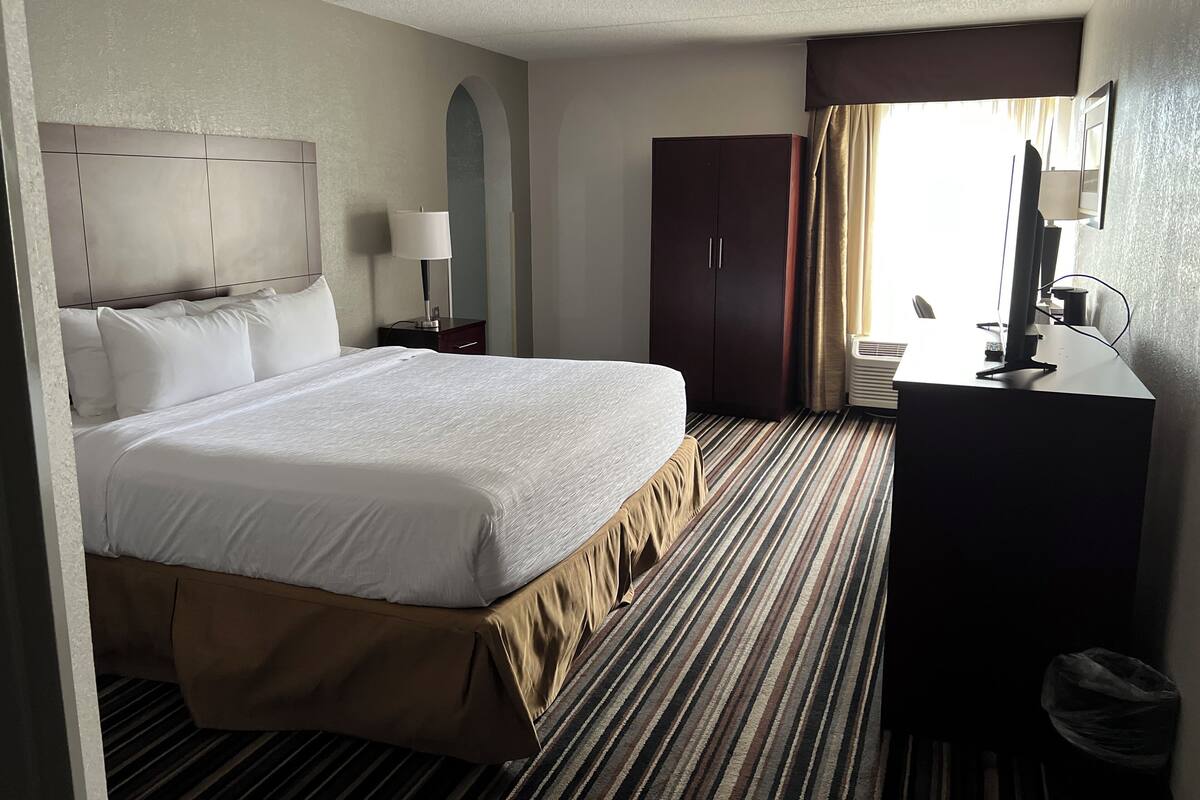 Une chambre d’hôtel avec un grand lit, un bureau avec un ordinateur, une armoire et une fenêtre avec des rideaux.