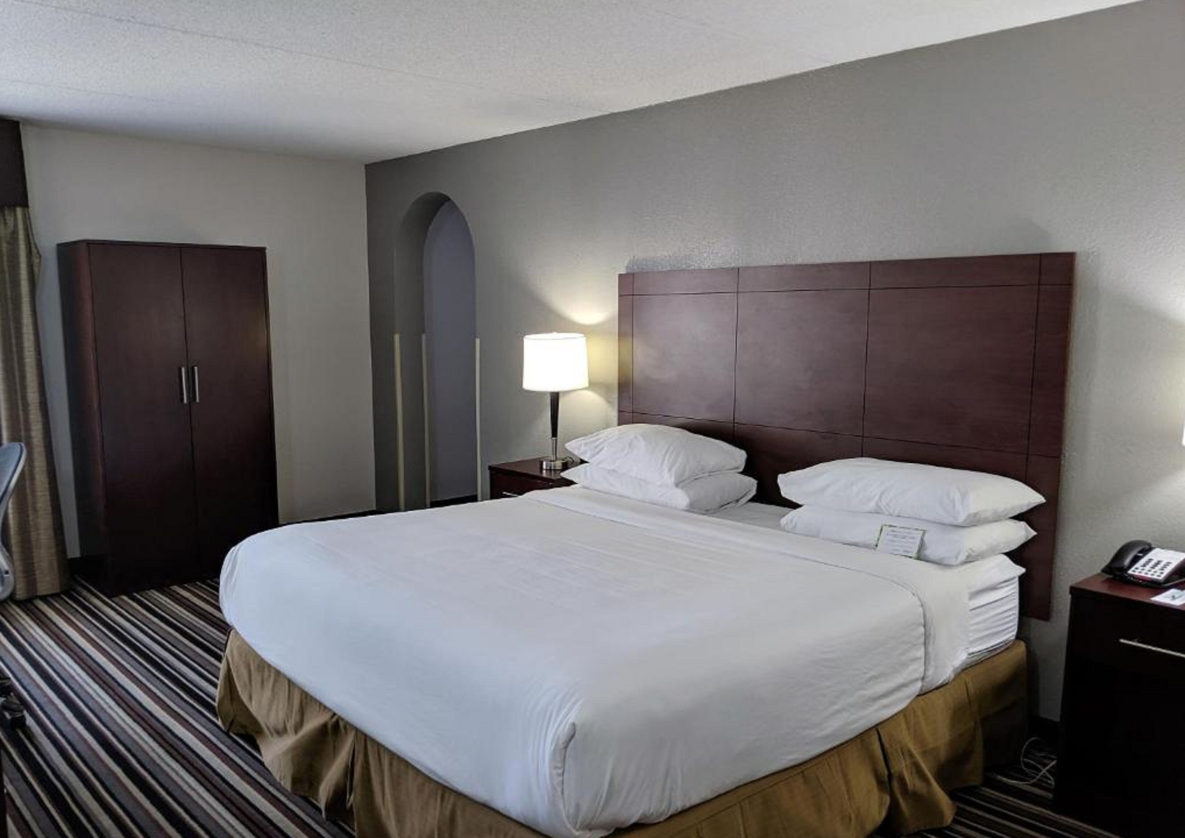 Ein Hotelzimmer mit einem großen Bett, einem Schrank, einem Nachttisch mit Lampe und einem Telefon.