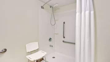 A white, accessible shower room with a grab bar, a white chair, and a showerhead.
