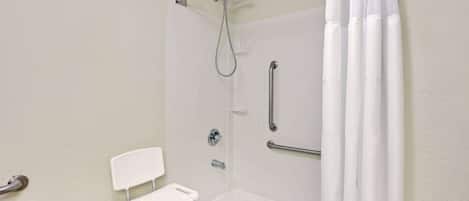 A white, accessible shower room with a grab bar, a white chair, and a showerhead.