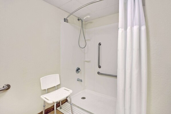 Baño accesible con ducha blanca, barra de apoyo, silla blanca y cabezal de ducha.