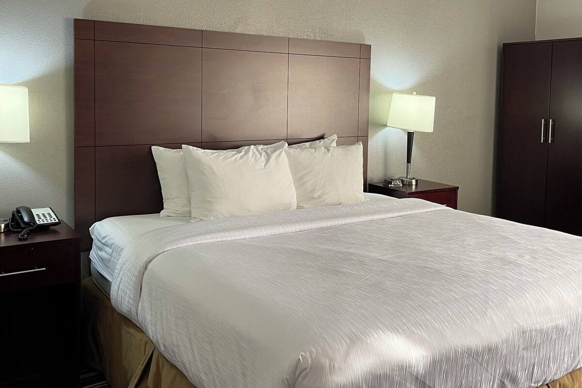 Une chambre d’hôtel avec un grand lit, deux tables de chevet avec des lampes, un téléphone et une armoire.