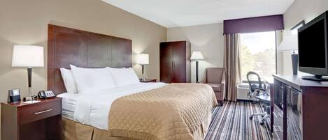 Une chambre d’hôtel comprenant un lit, des tables de chevet, un bureau avec une chaise, une télévision et une fenêtre avec des rideaux.