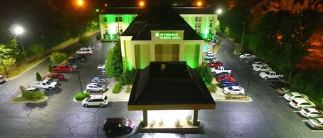 A Wyndham Garden Hotel with a parking lot full of cars and a green-lit building facade.