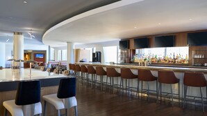 A modern bar area with a long counter, multiple bar stools, and a television screen. - Washington Dulles Airport Marriott (Sterling)