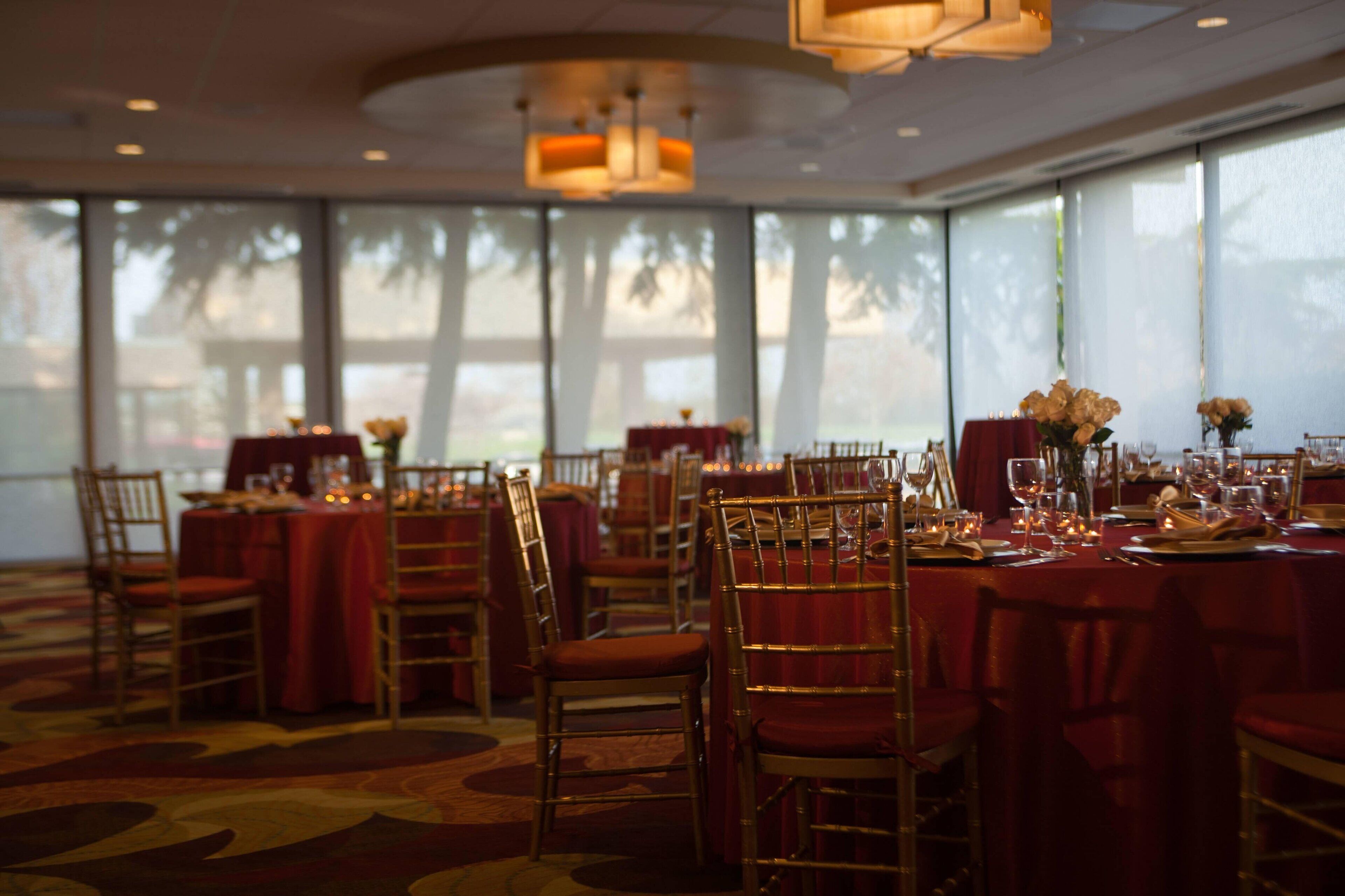 A banquet hall with round tables, red tablecloths, and gold chairs.