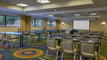 A conference room with tables and chairs, large windows, and a projector screen.