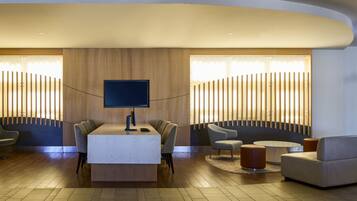 A modern lobby with a reception desk, seating area, and a large TV screen.