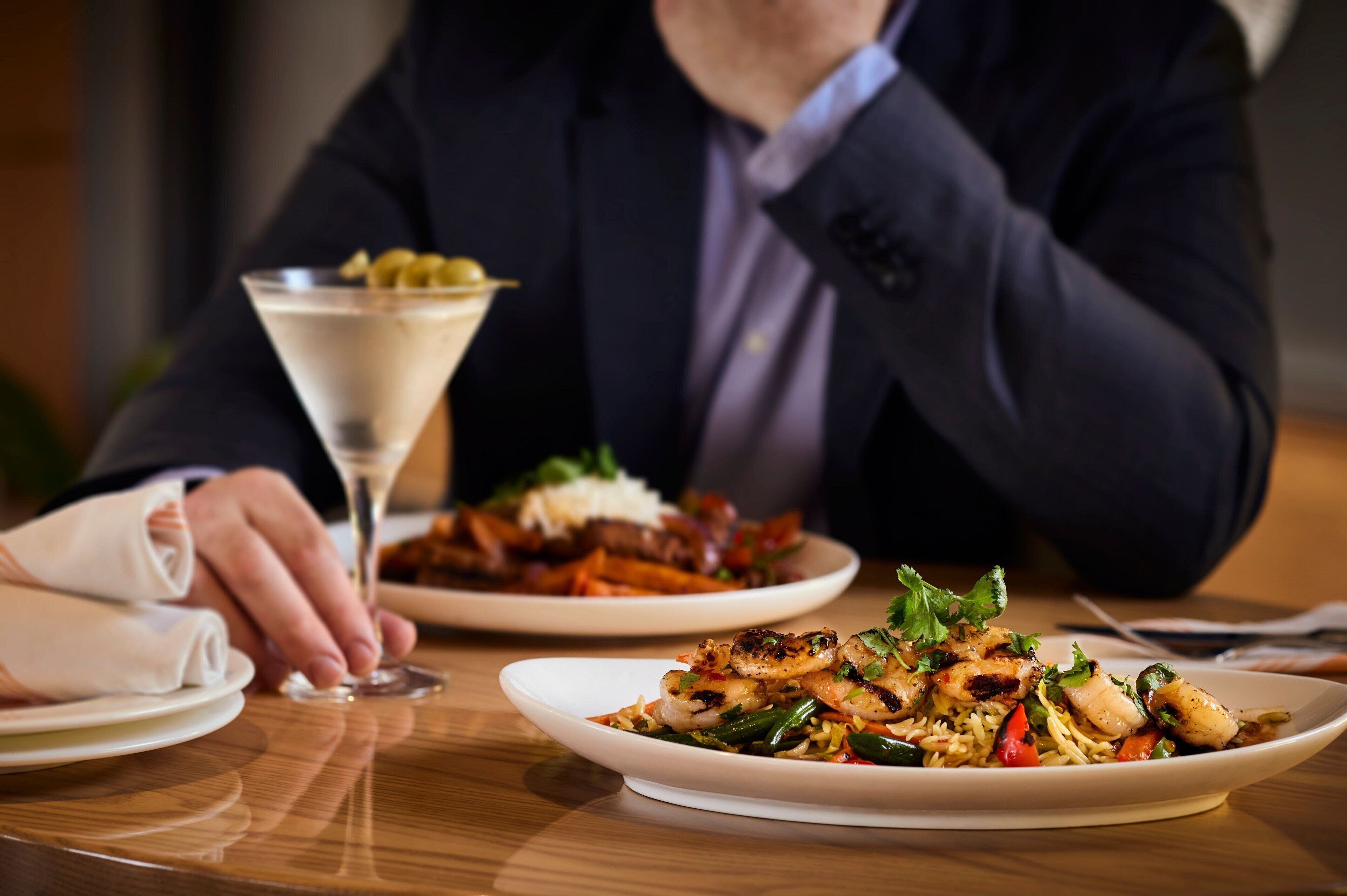 A dining table with plates of food and a martini glass.
