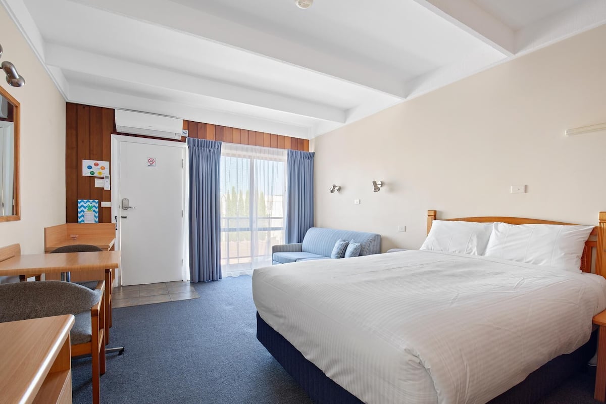 A hotel room with a bed, a desk, a chair, a sofa, and a door leading to a balcony.