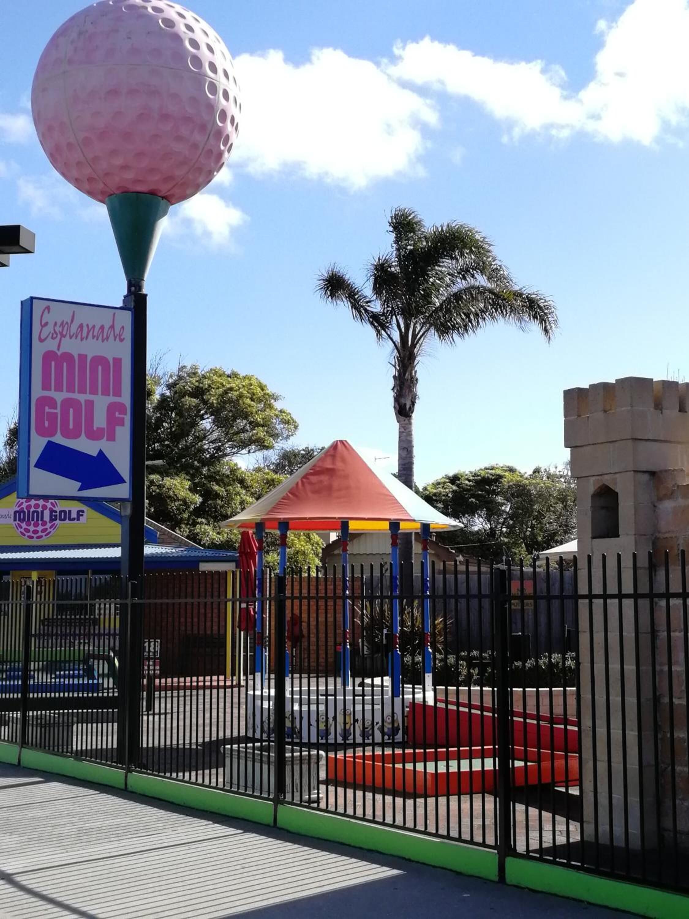 Un letrero de mini golf, una palmera y una estructura con forma de castillo.