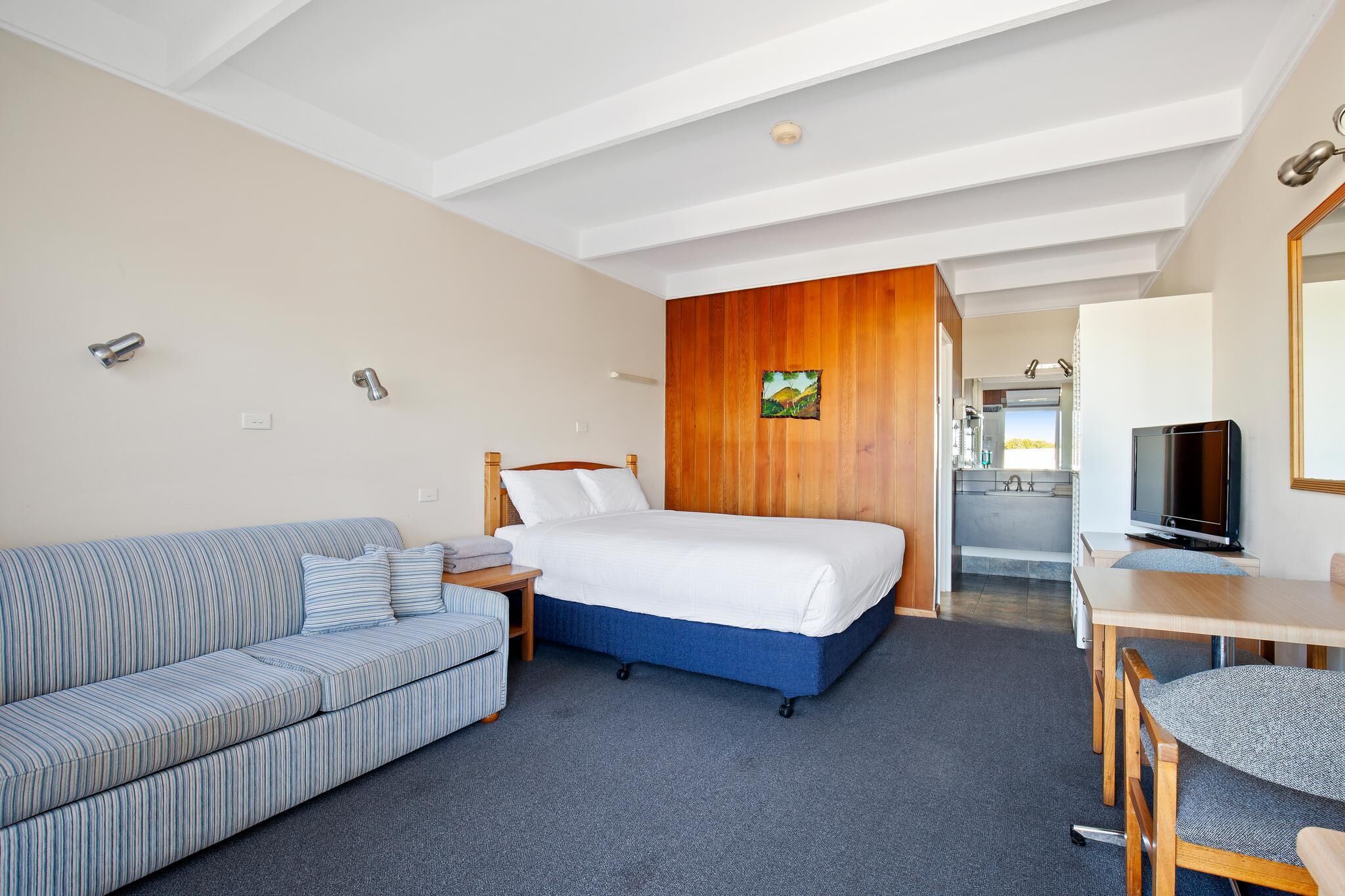 Quarto de hotel moderno com uma cama, um sofá, uma televisão e uma kitchenette pequena.