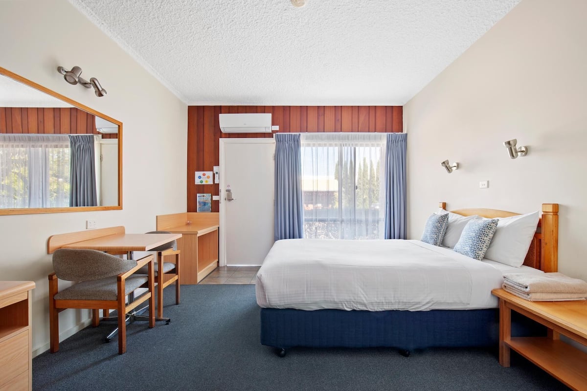 A hotel room with a bed, desk, chair, and a large window with curtains.