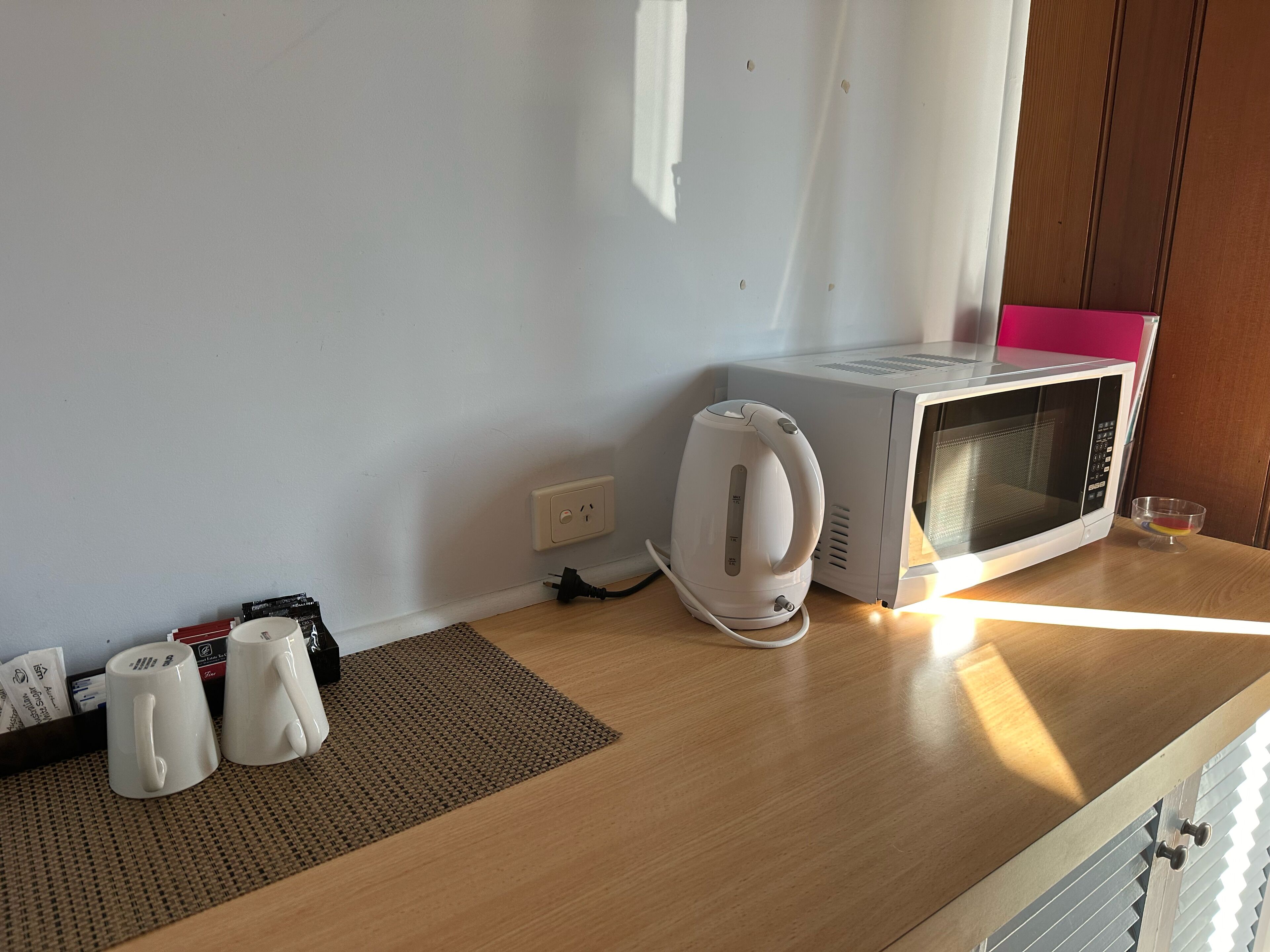 A kitchen with a microwave, kettle, and a small bowl on the counter.