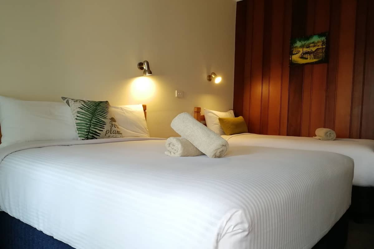 A hotel room with two beds, white linens, a green leaf-patterned pillow, and a painting on the wall.