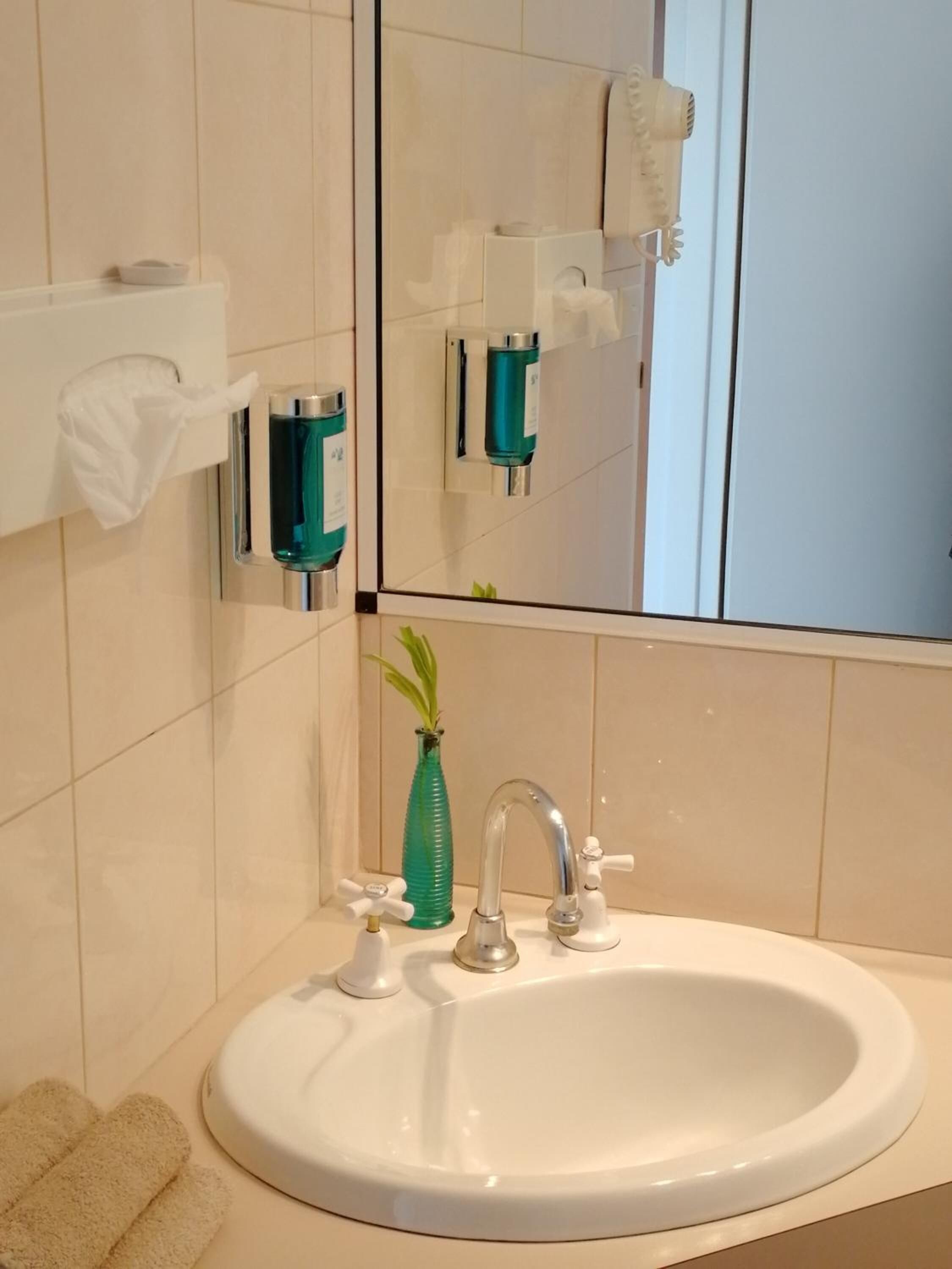 A bathroom with a white sink, a mirror, a green vase, and a towel rack.