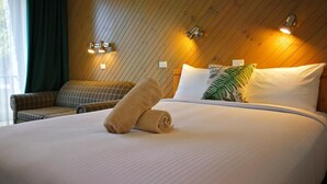 A hotel room with a large bed, a sofa, and a wooden wall with wall sconces. - Banjo Paterson Motor Inn (Lakes Entrance)