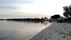A beach with footprints leading into the water, a calm lake, and buildings in the background. - Banjo Paterson Motor Inn (Lakes Entrance)