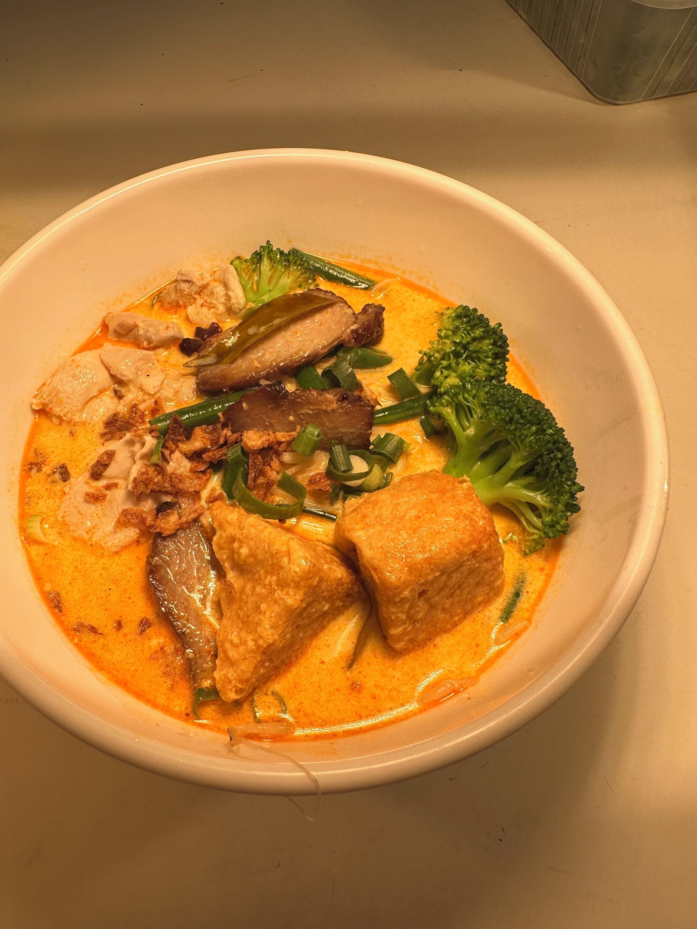 A bowl of soup with tofu, chicken, and vegetables.
