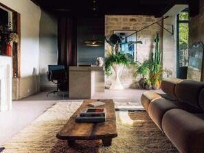 A modern living room with a sofa, a coffee table with books, a large potted plant, and a stone wall. - Hôtel Lulu Paris (Paris)