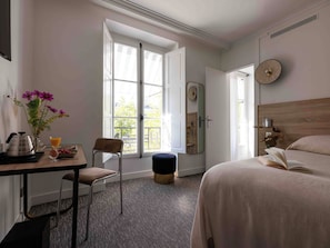 Une chambre à coucher avec un lit, une table de chevet sur laquelle se trouve un livre, une chaise, une fenêtre et une porte.