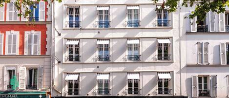 A multi-story building with balconies, large windows, and a storefront with a green awning.