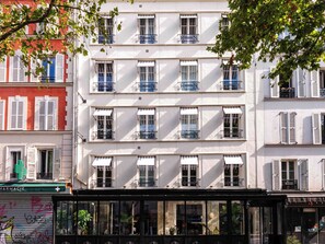A multi-story building with balconies, large windows, and a storefront with a green awning. - Hôtel Lulu Paris (Paris)