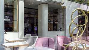A modern interior with round tables and pink chairs, glass display cases, and a decorative golden spiral. - Hôtel Nude Paris - Color Vision (Paris)