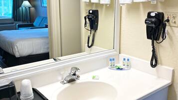 A hotel bathroom with a large mirror, two hair dryers, a sink, and toiletries.