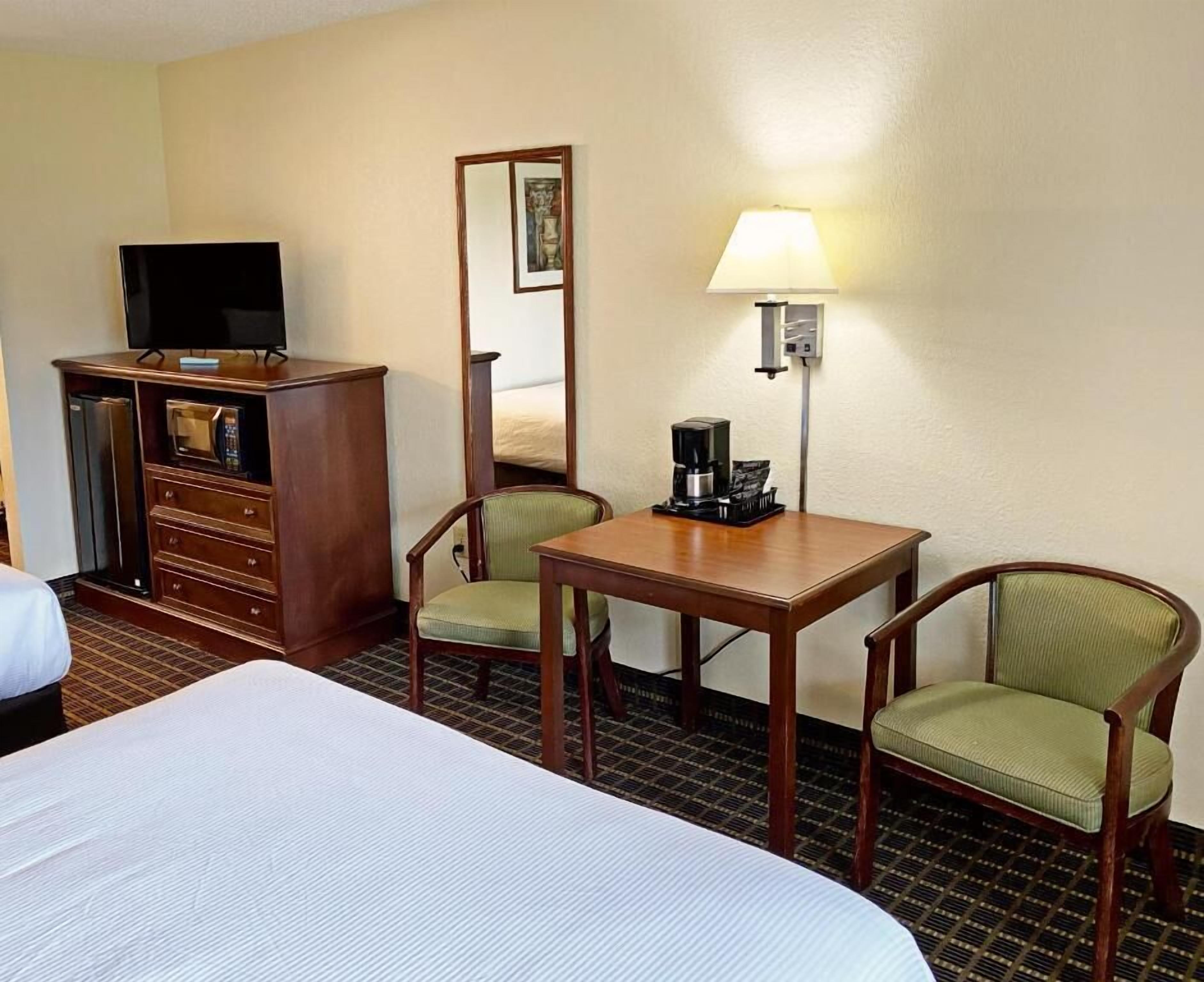 A hotel room with a bed, a desk with a lamp, a coffee maker, a television, and a dresser.