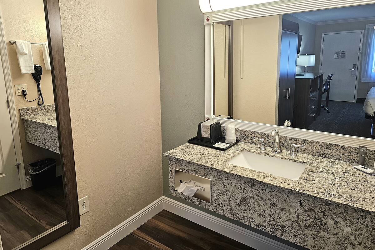 Un baño de hotel con encimera de granito, un lavabo, un espejo, un perchero para toallas y un teléfono.