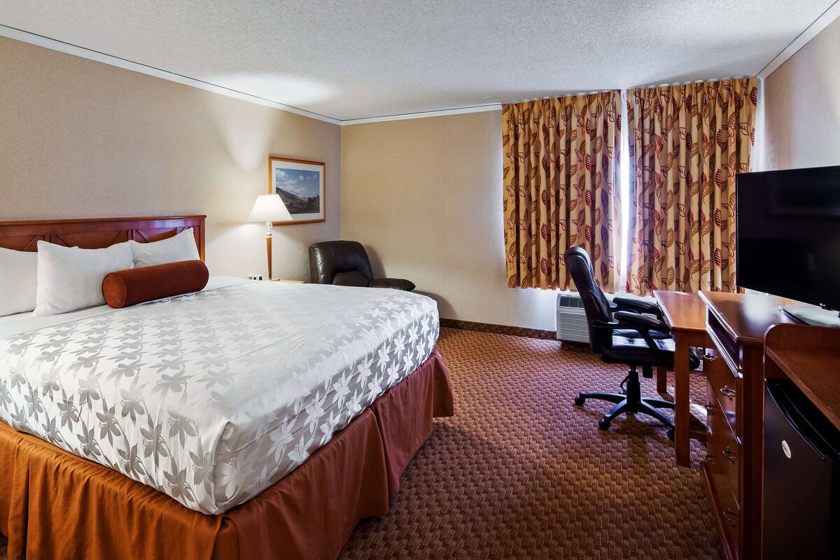 A hotel room with a large bed, a desk with a chair, a television, and a window with curtains.
