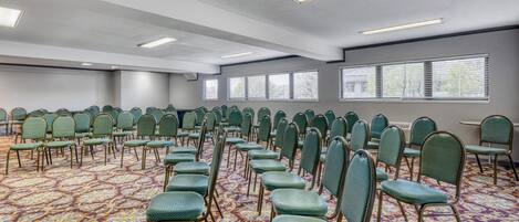A conference room with rows of green chairs, patterned carpet, and large windows.