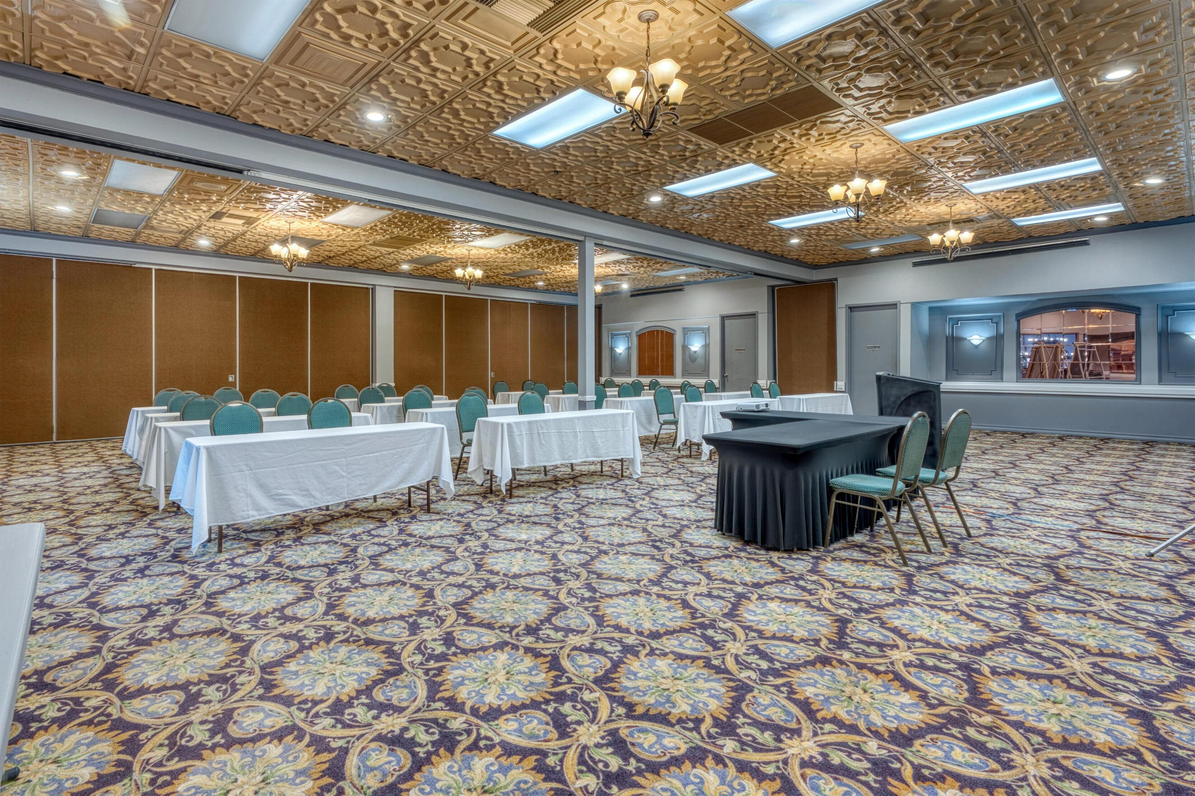 Un salón de conferencias con mesas y sillas, una alfombra estampada y un techo decorativo.