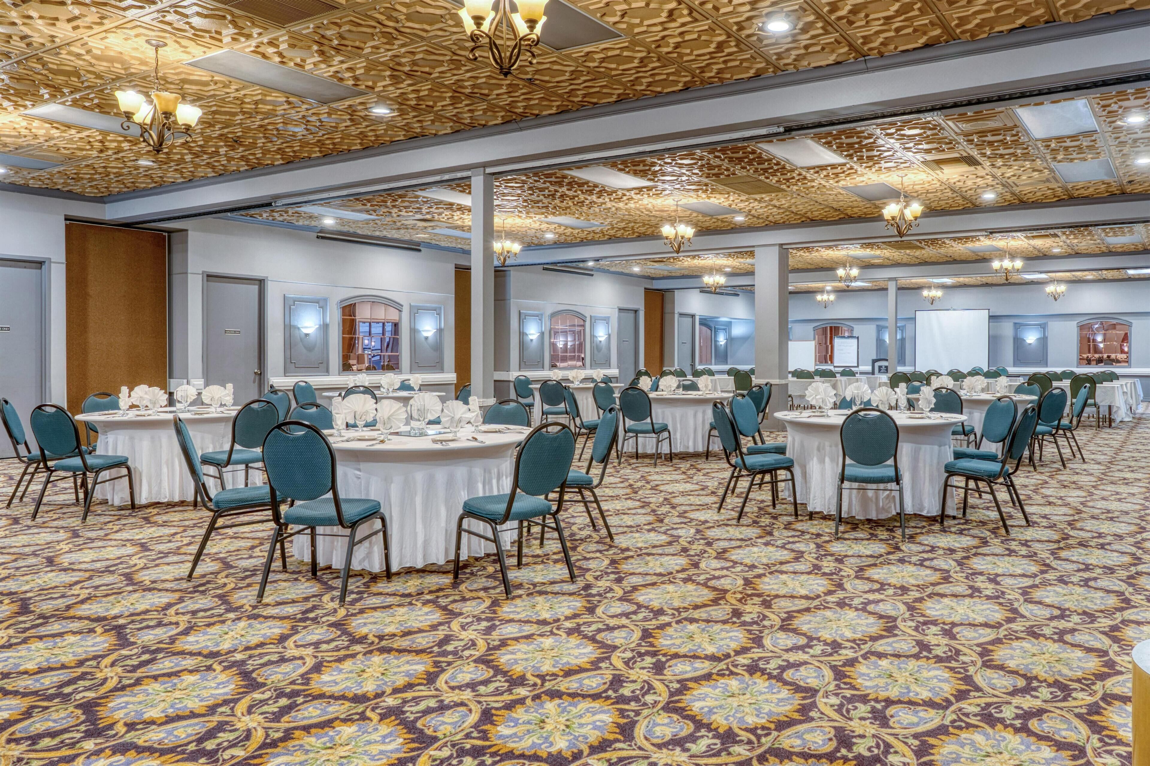 A banquet hall with round tables, teal chairs, and patterned carpet.