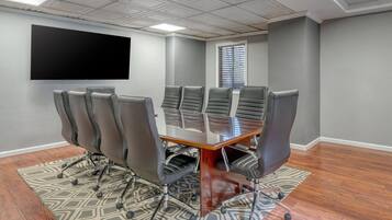 Un salón de conferencias con una televisión de pantalla plana grande, una mesa de cristal y seis sillas negras con ruedas.