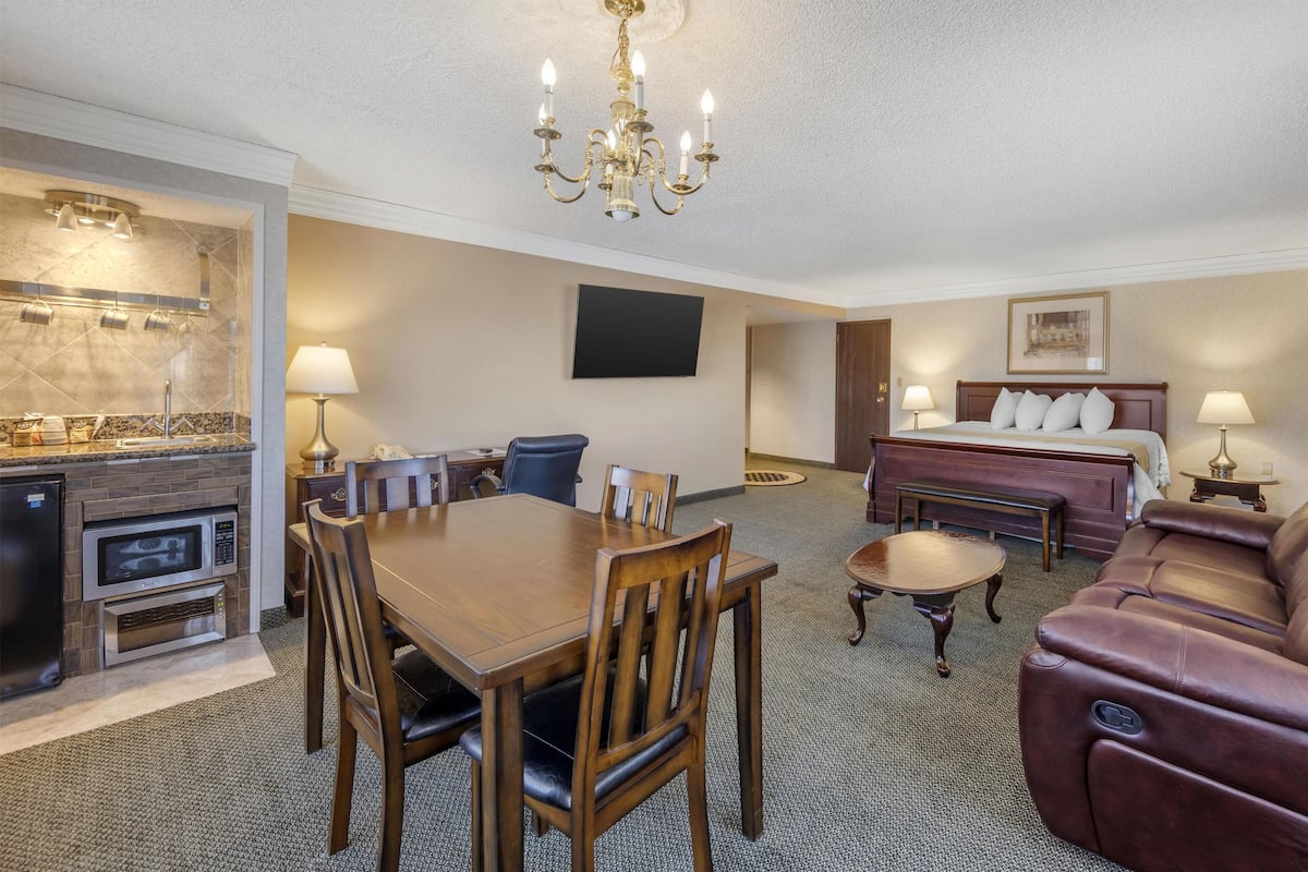A hotel room with a dining area, a kitchen, a living area with a sofa, and a bed.