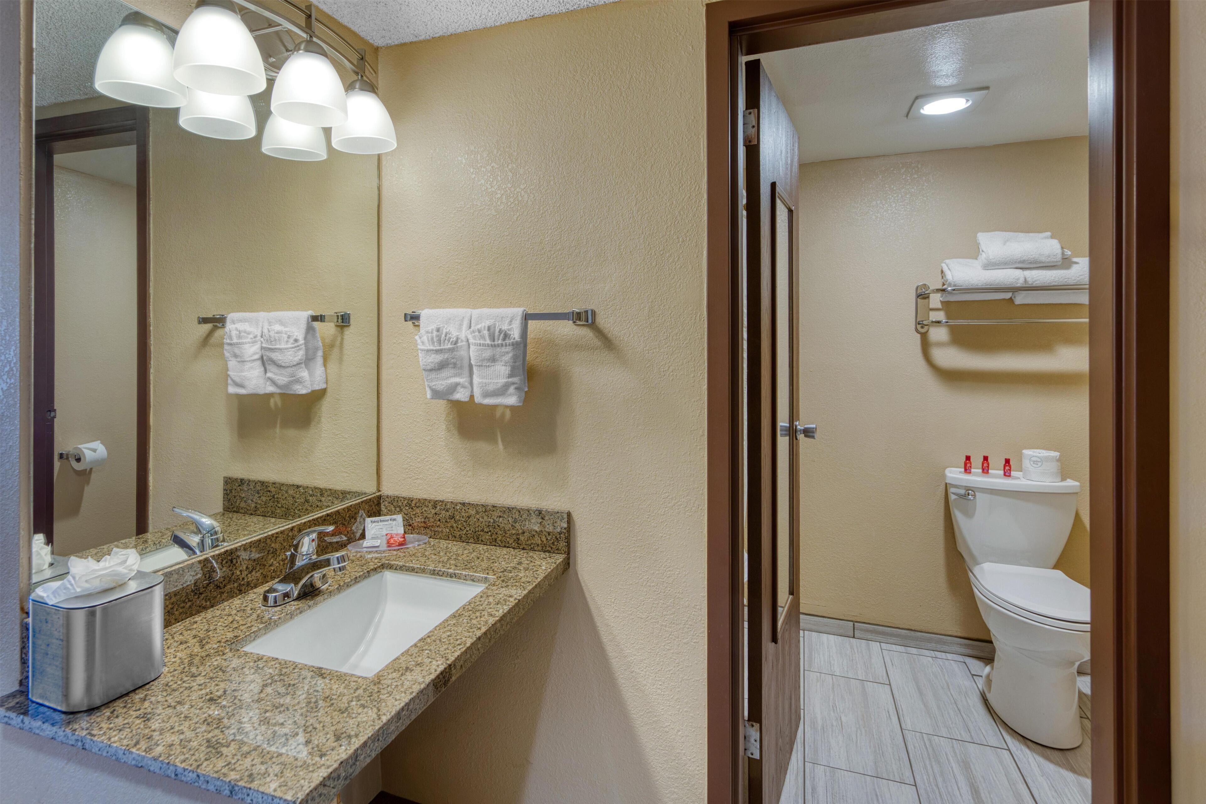 A bathroom with a granite countertop sink, a mirror, and a toilet.
