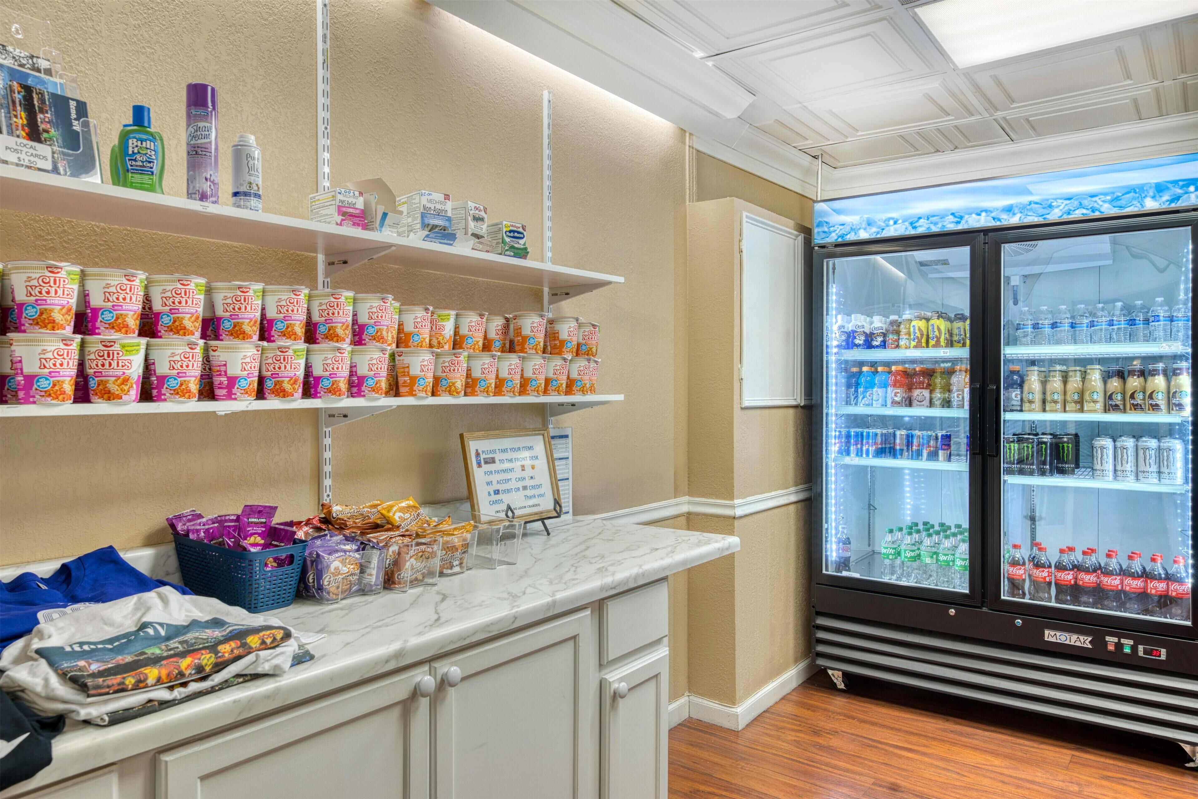 A hotel room with a marble countertop, a refrigerator stocked with beverages, and shelves with snacks and toiletries.
