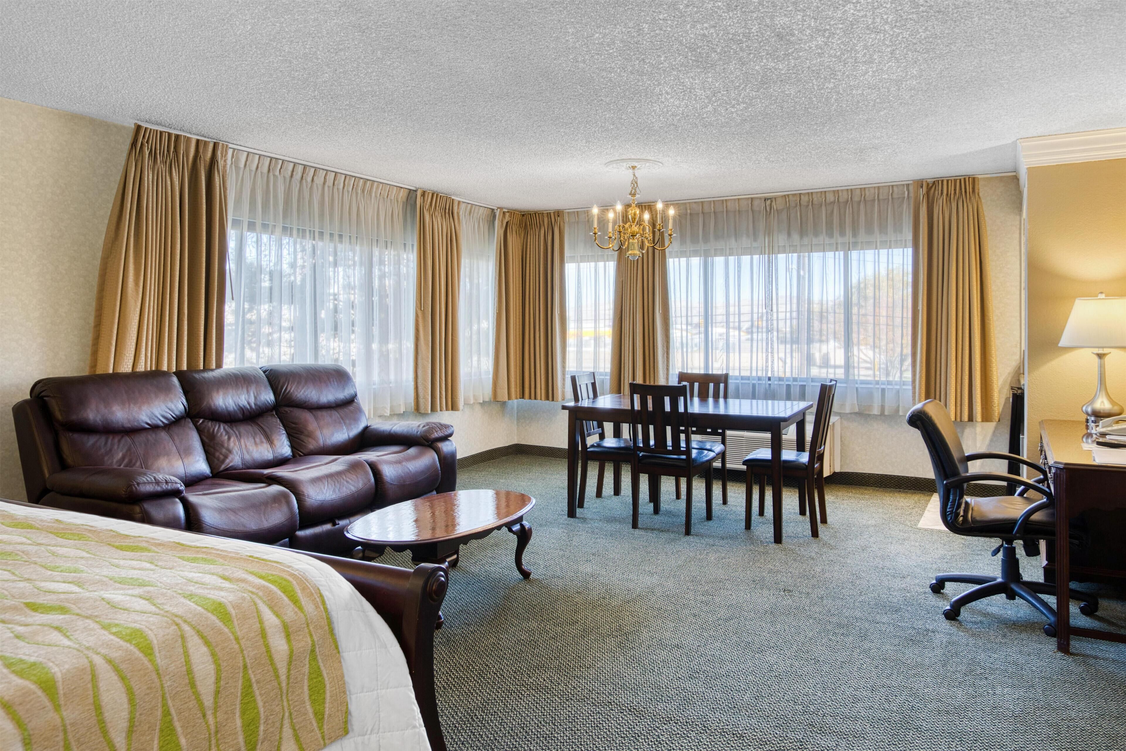 Et hotelværelse med en stor seng, en lædersofa, et spisebord med stole, et skrivebord med stol og en lysekrone.