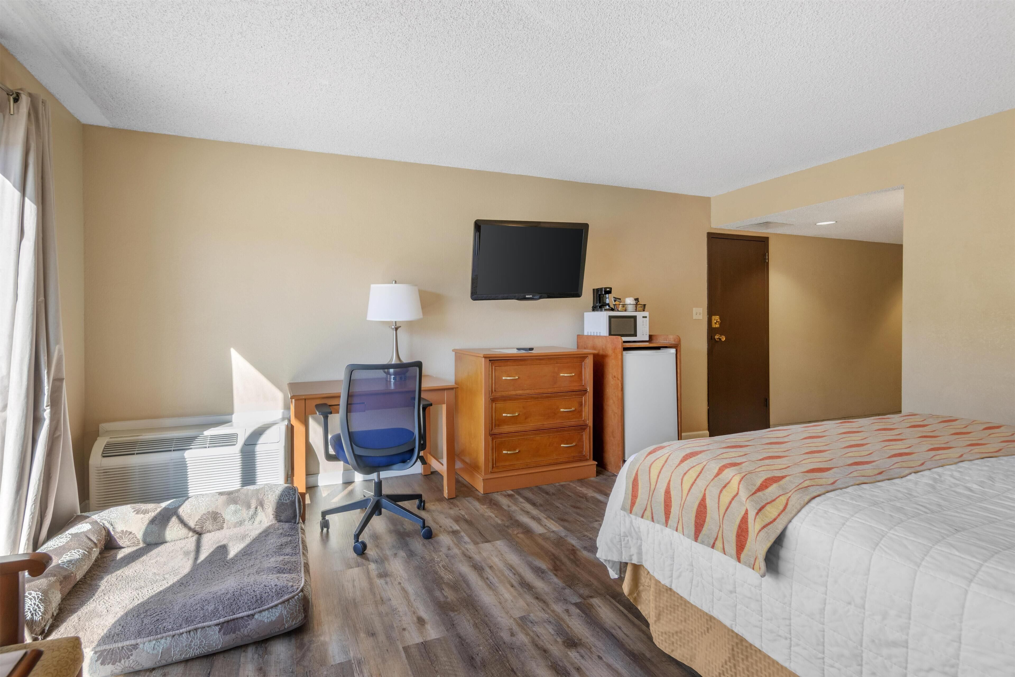 A hotel room with a bed, a desk with a chair, a television, a dresser, and a microwave.