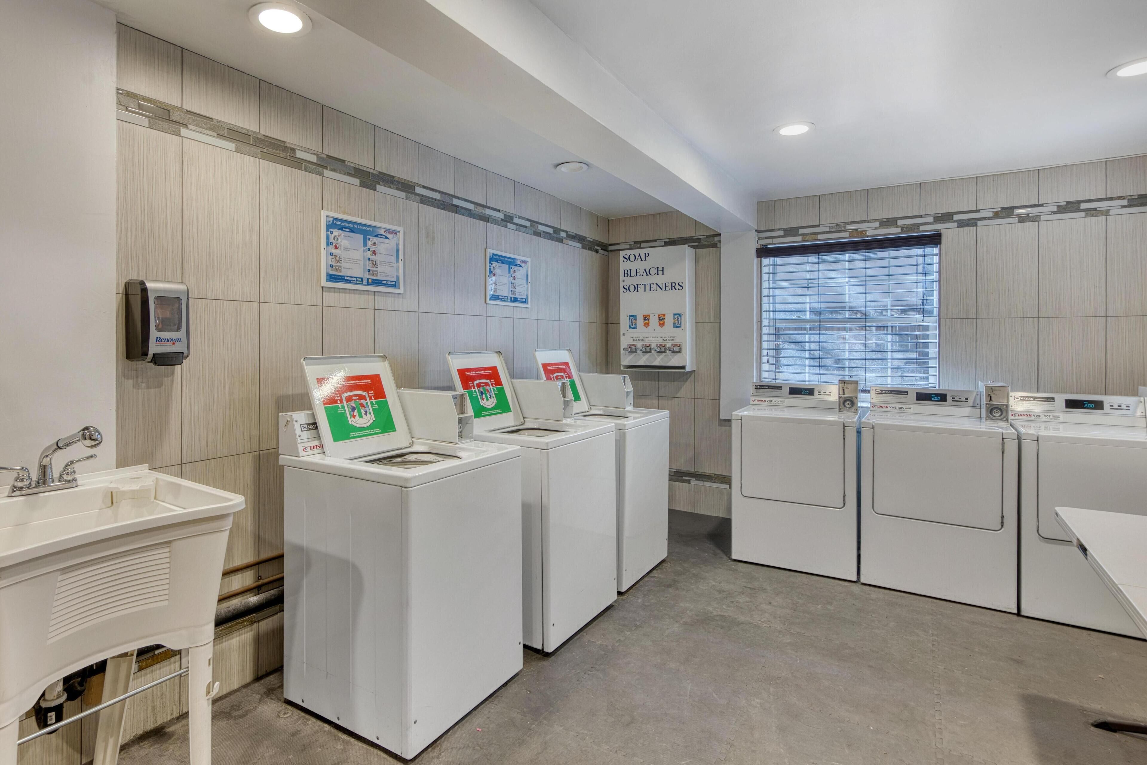 A laundry facility with multiple washing machines, a sink, and informational posters on the wall.