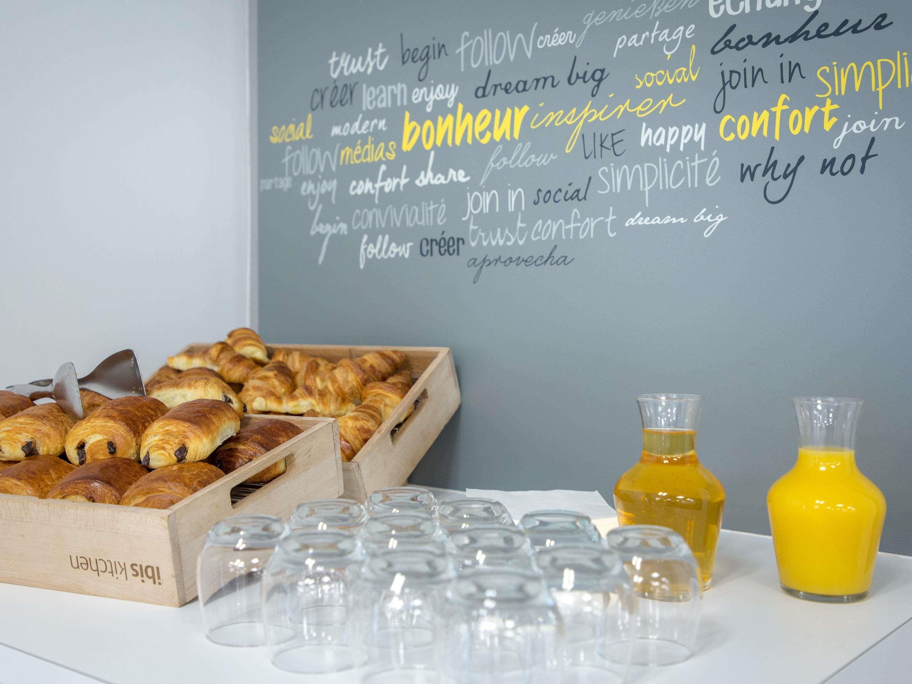 Ein Frühstückstisch mit Croissants, Gläsern und Orangensaftflaschen.