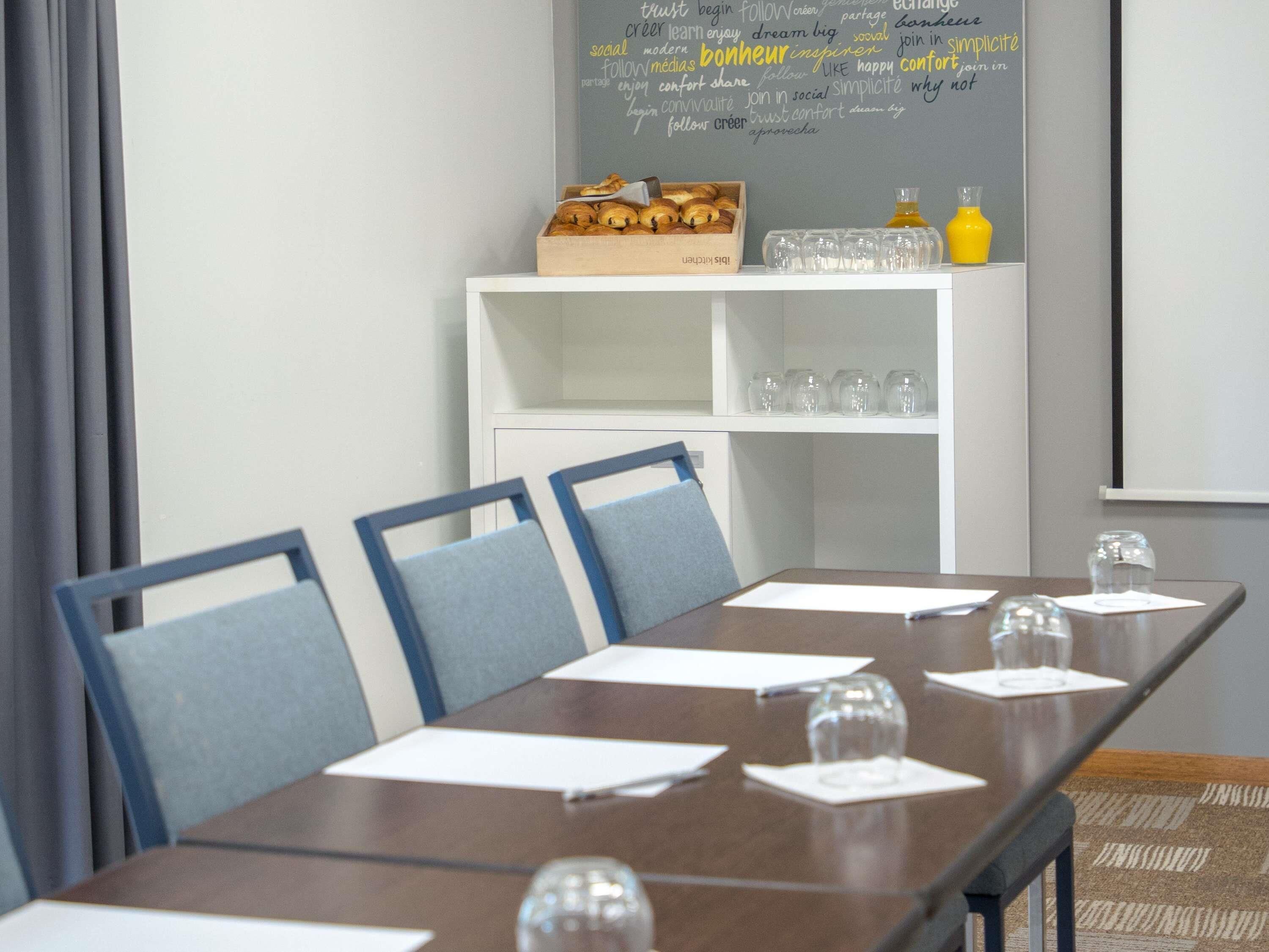 Een vergaderzaal met een lange tafel, stoelen, een whiteboard met motiverende zinnen en een plank met glazen en een fles.