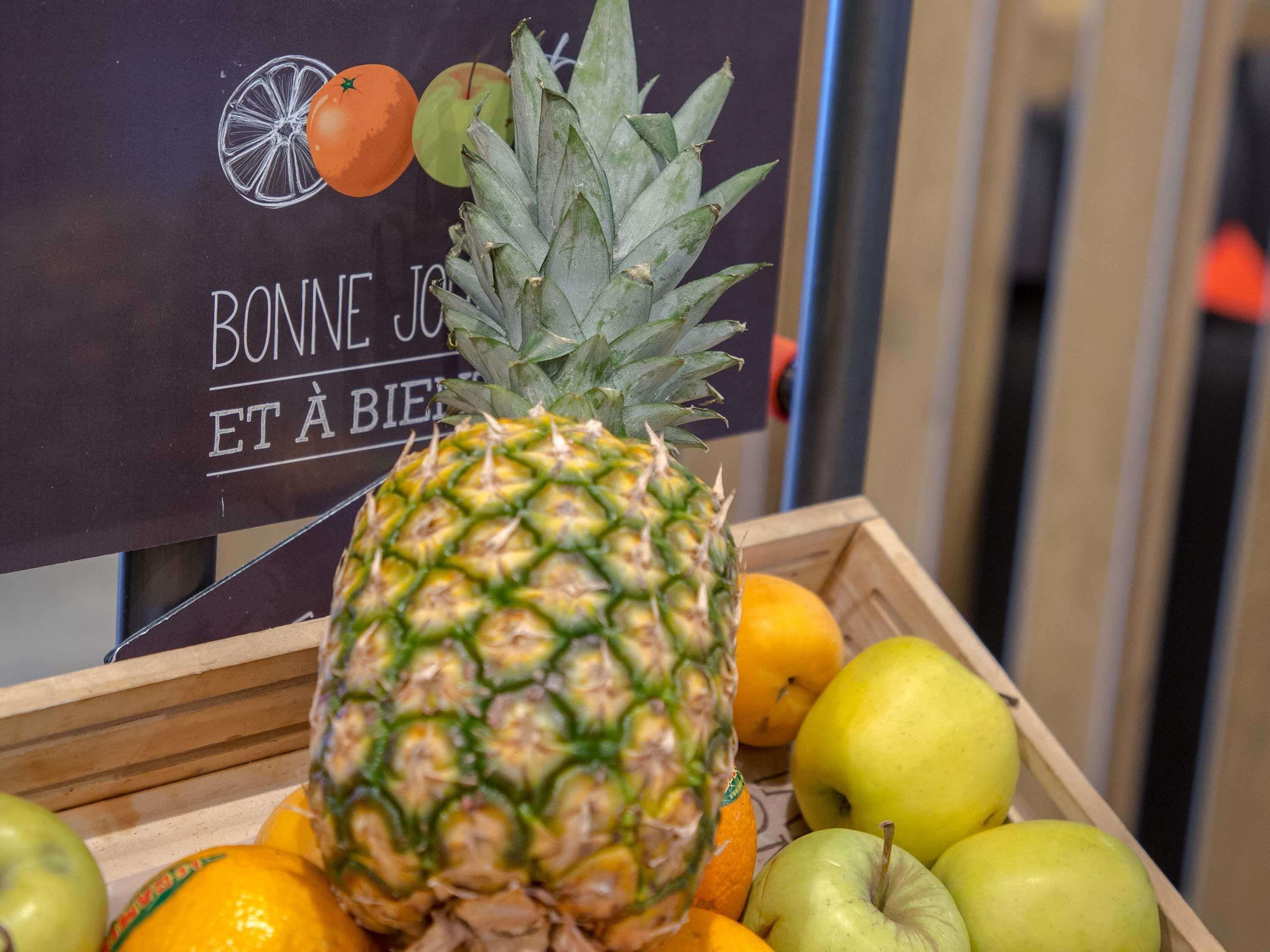 A wooden crate with a pineapple, oranges, and green apples.
