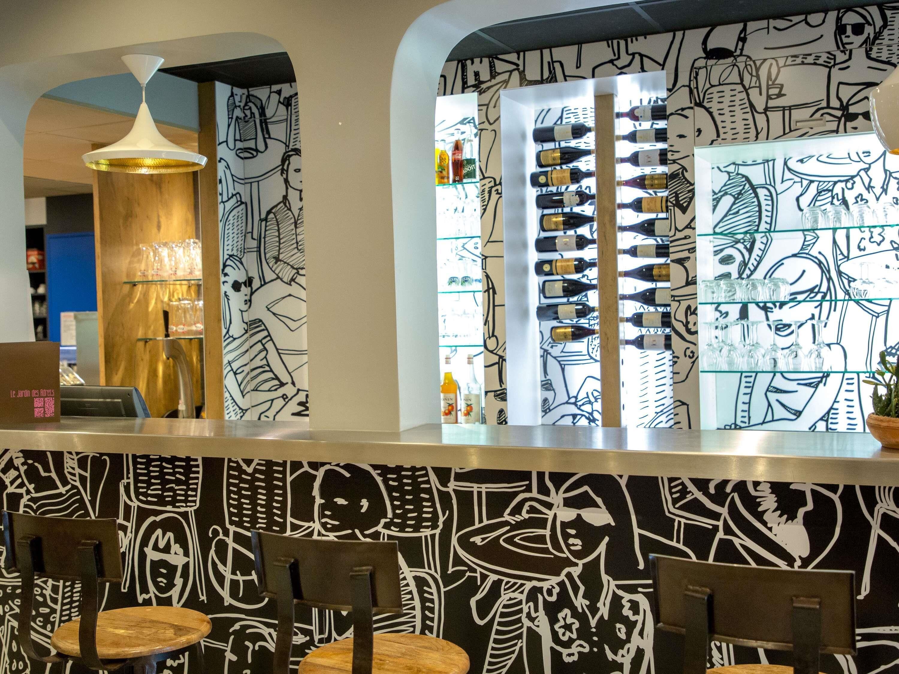A bar area with a black and white mural, a wine display, and wooden chairs.