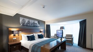 A hotel room with a large bed, a desk, a TV, a chair, and a window with curtains. - Bilderberg Garden Hotel (Amsterdam)