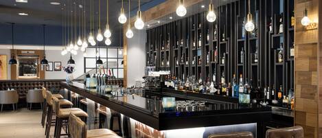 Una zona de bar con una barra larga, varios taburetes y una gran variedad de botellas y vasos.