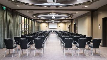 A conference room with rows of black chairs, a projector screen, and a large window with curtains.