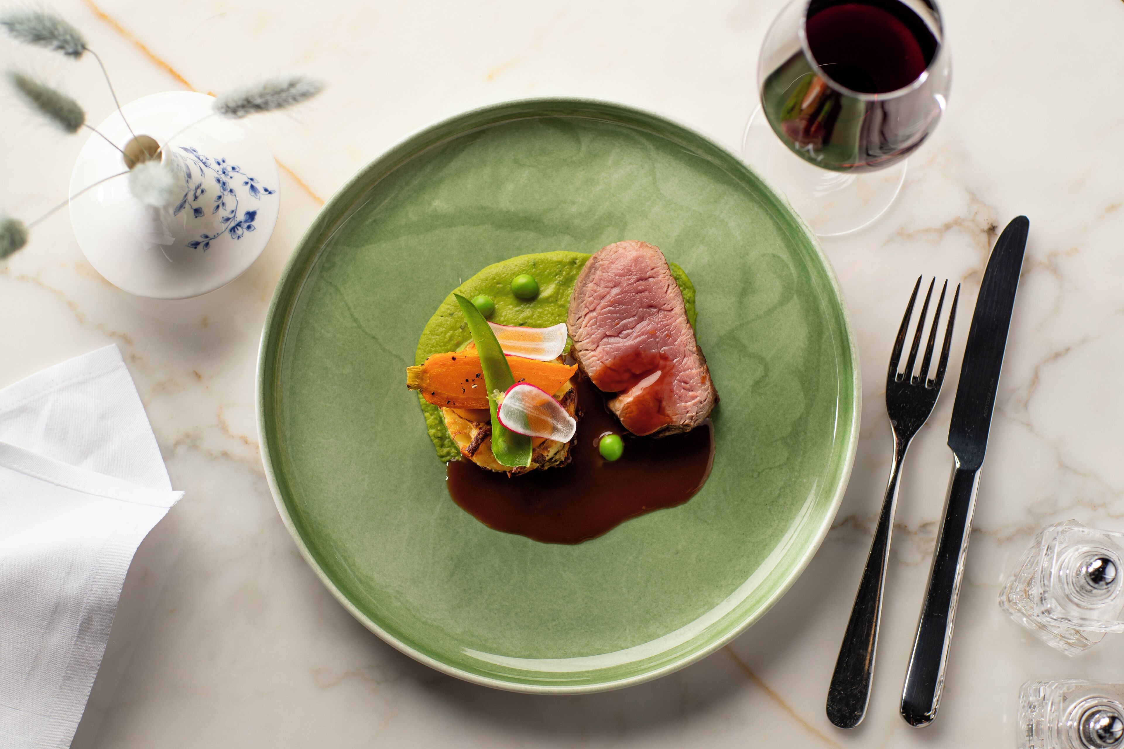 A plate with a green rim, containing a piece of meat, vegetables, and a green sauce.